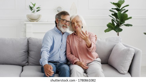 Caucasian Senior Man And Woman Woman On Retirement. Happy Couple Sitting On Sofa And Posing With Smiles To Phone Camera At Home. Old Couple Taking Selfie Photos With Smartphone.