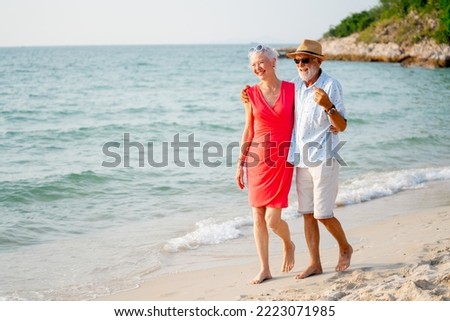 Caucasian senior man and woman walk along the beach together with evening warm light and they look relax and happy during vacation or holiday.