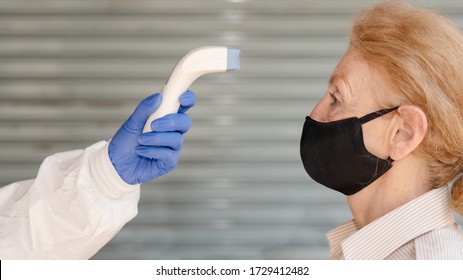 Caucasian Senior Woman Standing For Temperature Scanning With Digital Device For Fever Check In Coronavirus Covid-19 Spreading Prevention And Protection Method