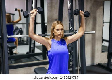 Caucasian serious young blonde woman lifting dumbbells in the gym alone - Powered by Shutterstock