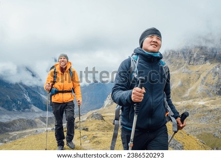 Caucasian and Sherpa men backpackers with trekking poles together hiking and enjoying Mera peak climbing acclimatization walk Makalu Barun Park route. Men enjoying Togetherness and beautiful valley.