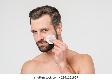 Caucasian Shirtless Young Man Using Cotton Pad For Applying Removing Makeup, Doing Face Cleaning Hygiene, Using Aftershave Cosmetics For Male Beauty Isolated In White Background