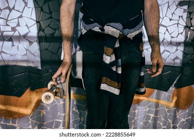 caucasian skater boy in a striped jumper tied at the waist holding a skateboard with his hand next to the wall of a tunnel - Shutterstock ID 2228855649