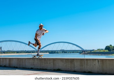 Caucasian Skater Guy Riding Skateboard With Beautiful Cityscape With River In The Background