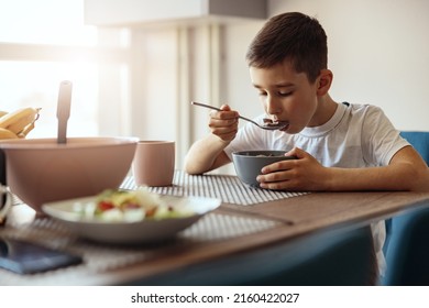 Caucasian Small Teen Boy Eating Cereals With Milk And Drinking Tea At Table In Morning.