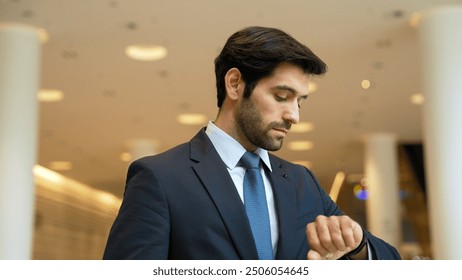 Caucasian smart business man looking at watch while waiting colleague. Executive manager wearing suit while standing at mall with blurred background. Investor wear blue suit check time. Exultant. - Powered by Shutterstock