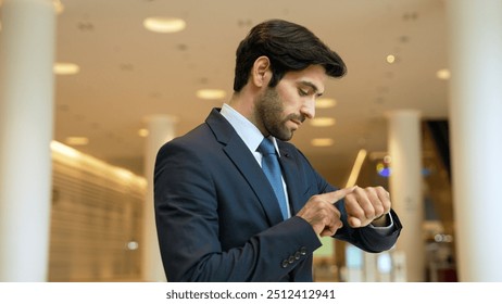 Caucasian smart business man looking at watch while waiting colleague. Executive manager wearing suit while standing at mall with blurred background. Investor wear blue suit check time. Exultant. - Powered by Shutterstock