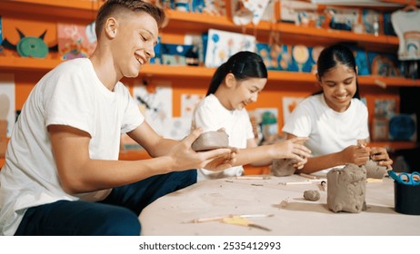 Caucasian smart teenager modeling clay while craving glass of clay at art lesson. Group of multicultural happy student working at dough in pottery workshop. Creative activity concept. Edification. - Powered by Shutterstock