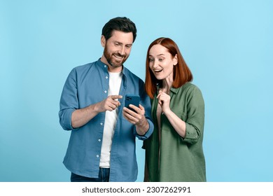 Caucasian smiling adult couple using mobile phone, scrolling news feed, checking social media content, texting online messages, checking new mobile application. Isolated blue color studio background - Powered by Shutterstock