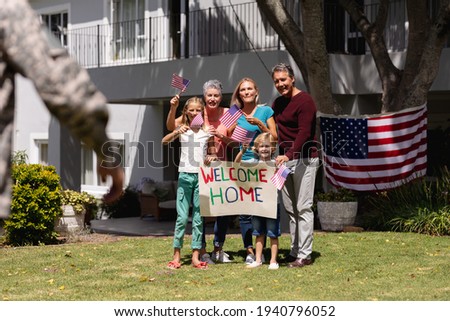 Caucasian soldier father and family meeting outside home with welcome sign and american flags. soldier returning home to family.