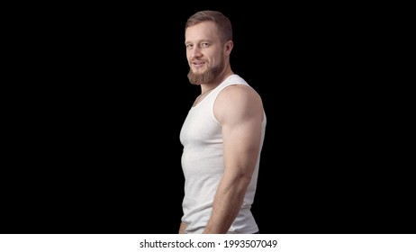Caucasian sporty man stands sideways in a tank top on a black background. One man is a model. High quality photo - Powered by Shutterstock