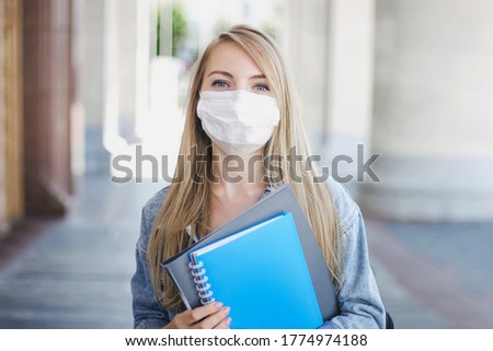 Caucasian student girl wearing a medical mask holds exercise book in her hands and looks to the camera, the new rules for education during the coronovirus quarantine, a pandemic in schools