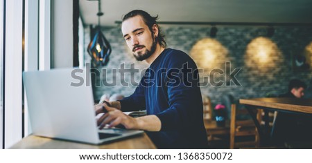 Caucasian student watching webinar on laptop computer improving skills on programming, serious professional web designer working on freelance sitting in cafeteria and using good wifi connection