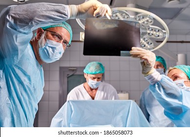 Caucasian Surgical Team Talking About X-ray In An Operating Theater, Discuss X-ray Before Interfere With Body Surgery, Check The Lungs. Coronavirus, Covid-19 Concept