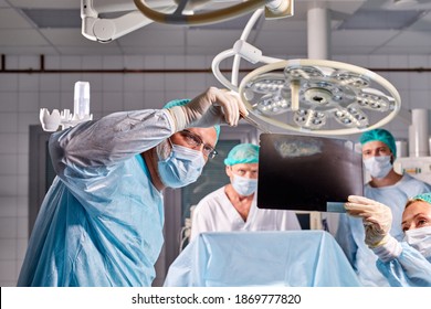 Caucasian Surgical Team Talking About X-ray In An Operating Theater, Discuss X-ray Before Interfere With Body Surgery, Check The Lungs. Coronavirus, Covid-19 Concept