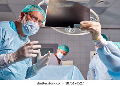 Caucasian Surgical Team Talking About X-ray In An Operating Theater, Discuss X-ray Before Interfere With Body Surgery, Check The Lungs. Coronavirus, Covid-19 Concept