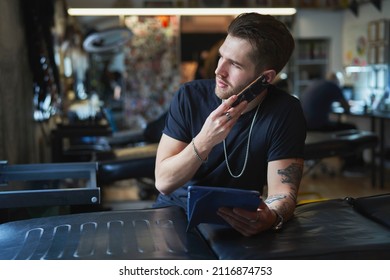 Caucasian Tattoo Artist Talking By Mobile Phone And In Tattoo Studio