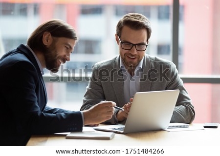 Caucasian teammates two positive businessmen sitting at desk in modern office looking at computer screen using learn new corporate e-business application, modern technology business management concept
