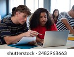 Caucasian teen boy and black teenage female high school students in class working together on school project using laptop.