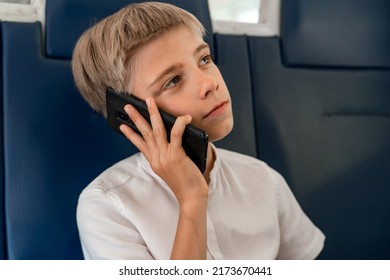 Caucasian teen boy sitting talking on phone while traveling by train. Kid is talking on a smartphone on a trip.