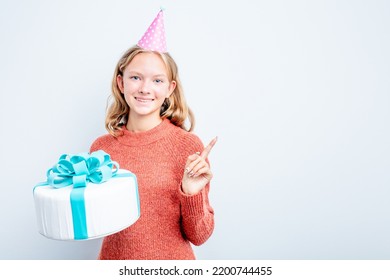 Caucasian Teen Girl Holding A Cake Isolated On Blue Background Smiling And Pointing Aside, Showing Something At Blank Space.