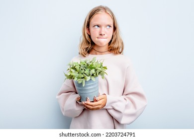 Caucasian Teen Girl Holding A Plant Isolated On Blue Background Confused, Feels Doubtful And Unsure.