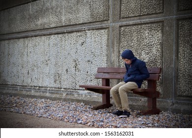 Caucasian teenage boy alone on a wooden bench next to a concrete wall