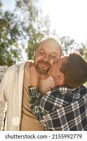 Caucasian teenage boy with cerebral palsy kissing smiling adult father in sunny day. Family relationship and spending time together. Disability care and rehabilitation. Fatherhood and parenting