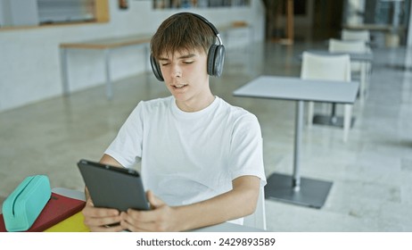 Caucasian teenage boy with headphones using tablet in modern university library. - Powered by Shutterstock