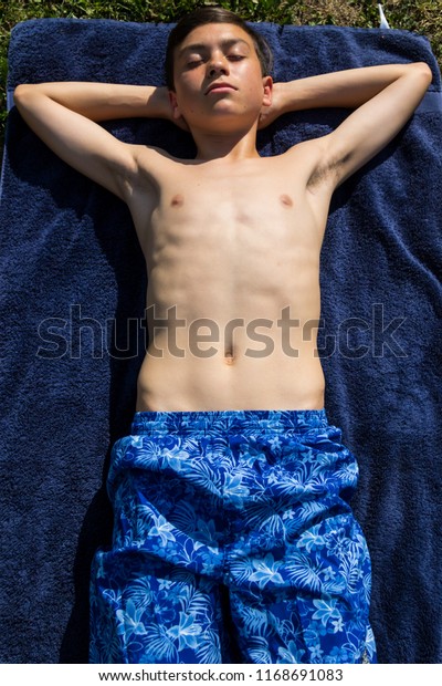 Caucasian teenage boy sunbathing in a garden wearing 