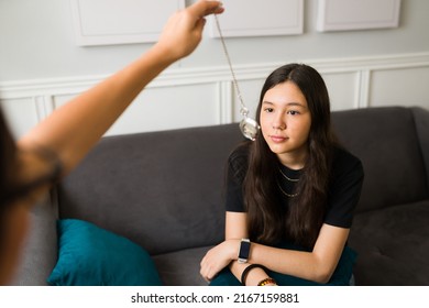Caucasian teenage girl looking at a clock to get hypnotized during a therapy session. Therapist hand using a clock to hypnotize a teen patient