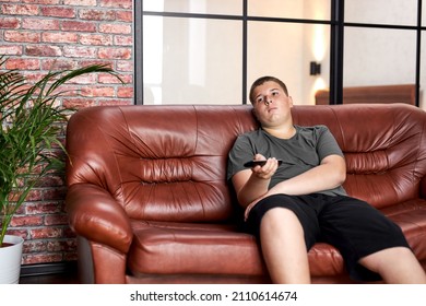 caucasian teenager boy laid on sofa watching tv. Relaxing thoughtful lifestyle portrait in t-shirt looking at television alone after school, lazy bummer. unhealthy lifestyle, need more activity