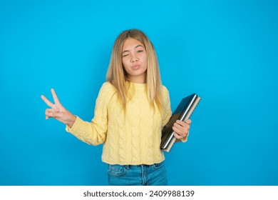 Caucasian teenager girl  makes peace gesture keeps lips folded shows v sign. Body language concept