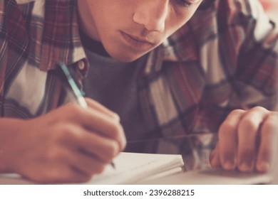 caucasian teenager indoor doing homework on the table at home - blonde guy writing and reading in his laptop or computer to get greats scores - portrait of boy with headphones - Powered by Shutterstock