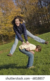 Caucasian teens one male and one female horsing around in a park playing leapfrog