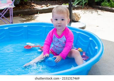 Caucasian Toddler Baby, Playing In The Kiddie Pool On A Sunny Summer Day. Sun Protection Baby Swimwear	