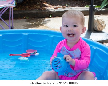 Caucasian Toddler Baby, Playing In The Kiddie Pool On A Sunny Summer Day. Sun Protection Baby Swimwear