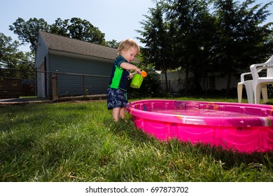 Caucasian Toddler Blonde Haired Boy Plays In A Pink Backyard Kiddie Pool During  A Hot Summer Day