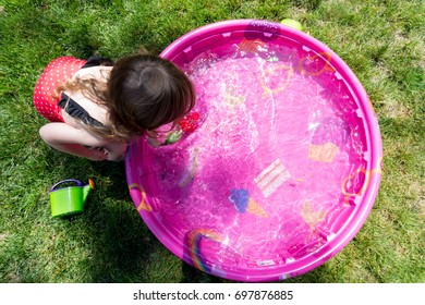 Caucasian Toddler Brown Haired Girl Plays In A Pink Backyard Kiddie Pool During  A Hot Summer Day