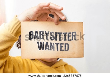 Caucasian toddler hand holding a yellowed flyer with Babysitter wanted written with stamp letters, baby care personnel for hire concept