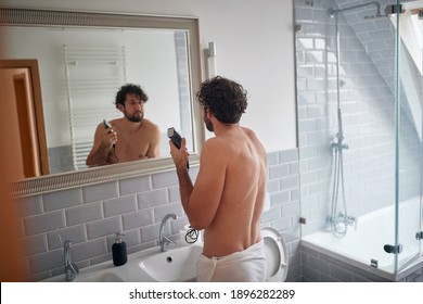 Caucasian topless man shaving with shaver in the bathroom