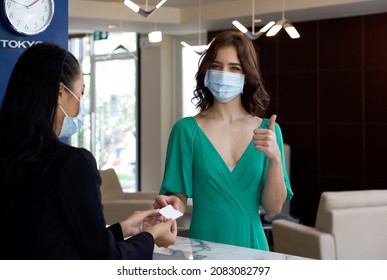 Caucasian Tourist In Green Cloth  Receiving A Room Card From Hotel Manager In Black Suit. Hotel Staff And Tourist Wear Face Mask To Protect Them From The Coronavirus Outbreak.