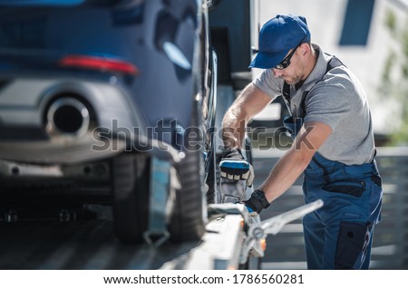 Caucasian Towing Company Worker inn His 40s Securing Modern Vehicle on the Towing Truck Platform. Cars Transportation Business.
