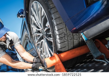 Caucasian Towing Truck Driver Securing Vehicle Cargo. Modern Car Towed Away. Repo Men Concept.