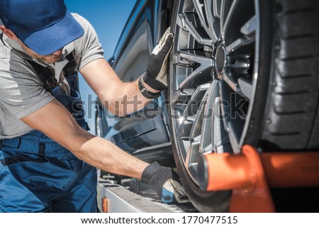 Caucasian Towing Truck Worker in His 40s Preparing For Car Shipment. Checking Cargo Support Equipment. Transportation Theme.