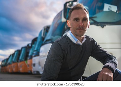 Caucasian Transportation Company Owner In His 40s And His Coach Buses Fleet In Background. Company Base Lot.