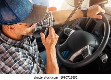 Caucasian Trucker In His 40s Making Conversation Using CB Radio Inside His Semi Truck Cabin. Convoy Truck Drivers Communication Theme.