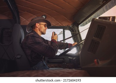 Caucasian Trucker Wearing Western Style Outfit Driving His Semi Truck And Talking Through CB Radio. Side View.