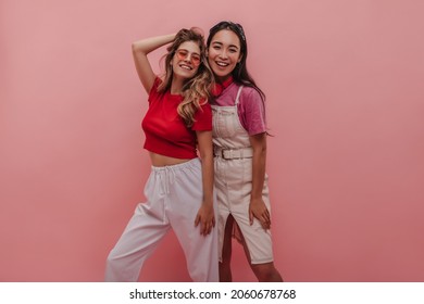 Caucasian And Ukrainian Young School Girl Friends Posing For Parents On Summer Vacation. Blonde With Wavy Hair And Red Crop Top With Girl In Denim Dress And Pink Shirt. Lifestyle Female Beauty Concept