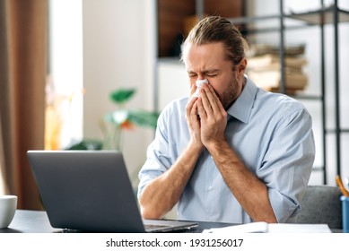 Caucasian Unhealthy Man Feeling Unwell, Sick With Running Nose, Need A Rest. Male Manager Or Freelancer Sit At The Desk At Home Office, Working Distantly, Using Paper Tissue, Sneezing